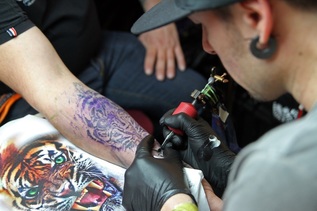 Tätowiere beim Stechen eines Tattoos - ein Tigerkopf.