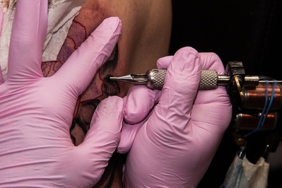 Detail - ein Tätowierer mit Einmalhandschuhen beim Stechen eines Tattoos